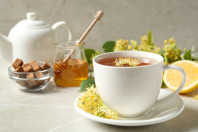 Photo of Cup of tea with linden blossom on light grey marble table