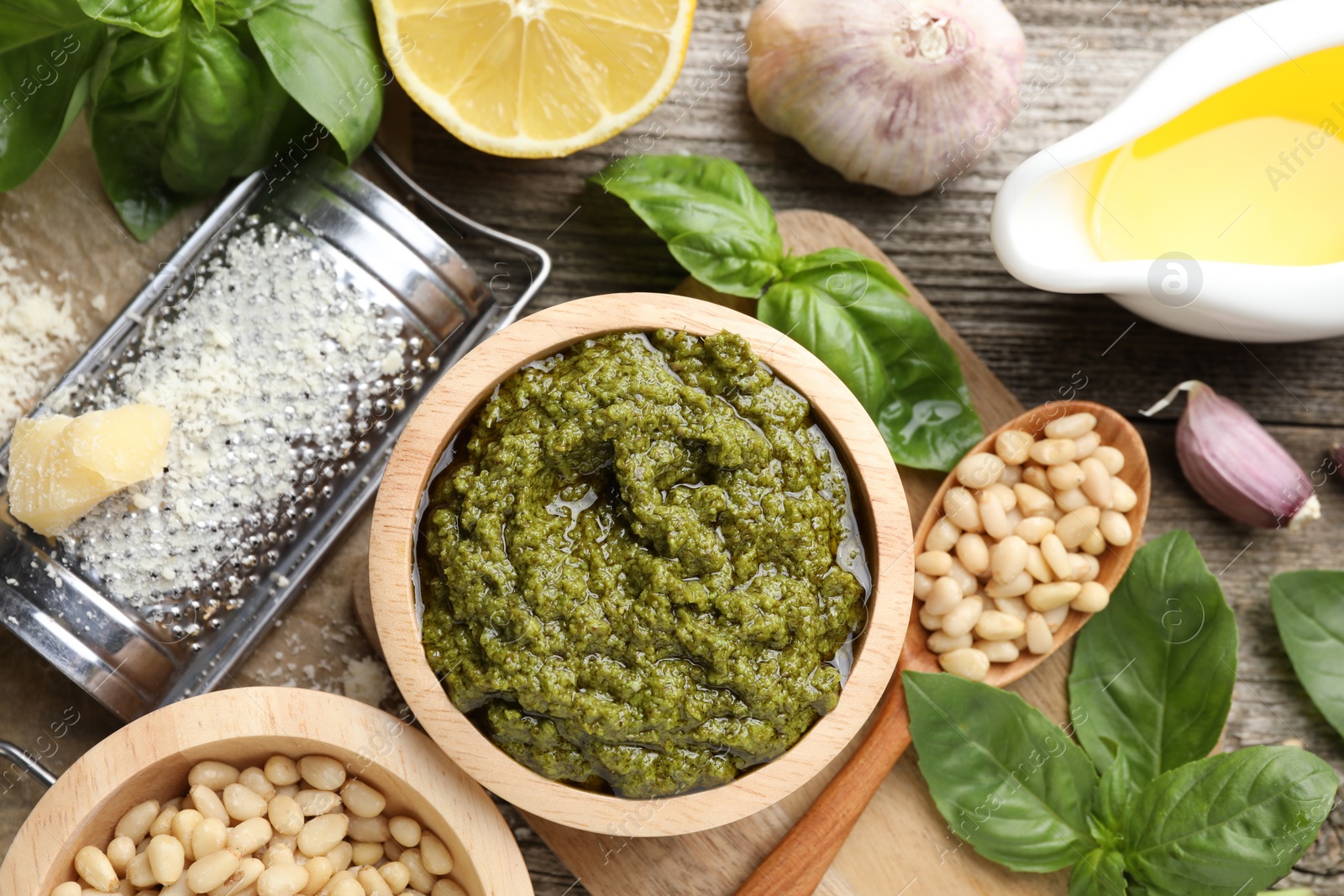 Photo of Tasty pesto sauce, basil, pine nuts, cheese, garlic and oil on wooden table, top view