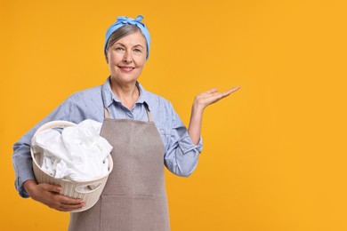 Photo of Happy housewife with basket full of laundry on orange background, space for text