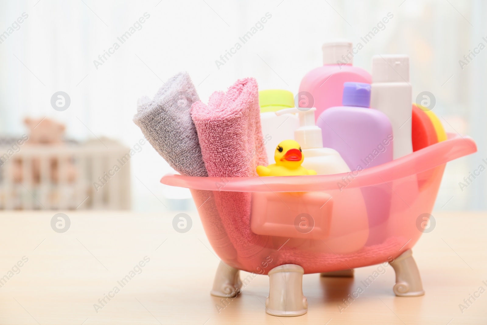 Photo of Baby cosmetic products, toy and towels on table indoors. Space for text