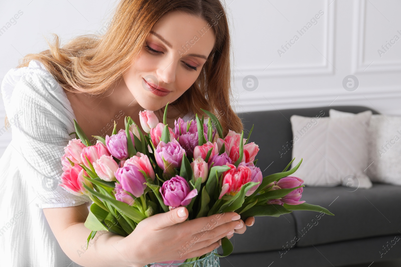 Photo of Young woman with bouquet of beautiful tulips indoors