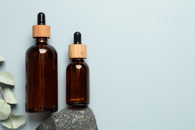 Photo of Flat lay composition with bottles of face serum, stone and eucalyptus branch on light grey background. Space for text