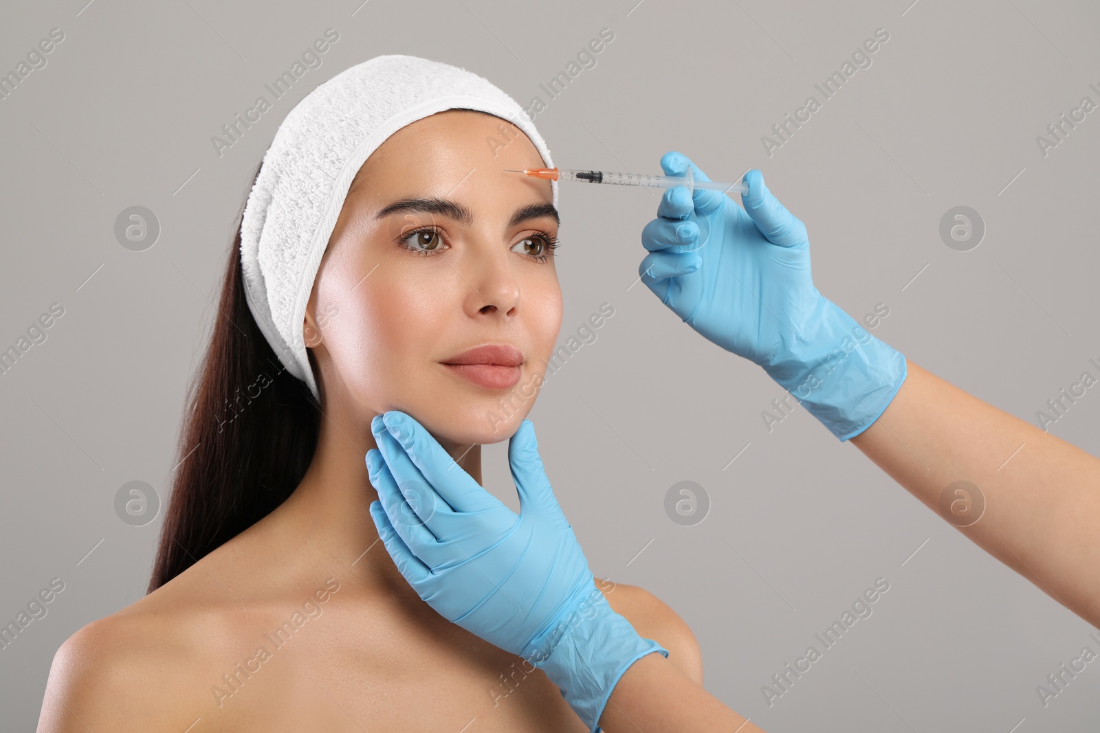 Photo of Doctor giving facial injection to young woman on light grey background. Cosmetic surgery