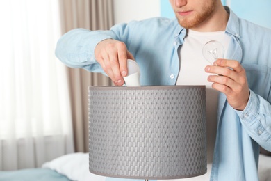 Photo of Man changing light bulb in lamp indoors, closeup