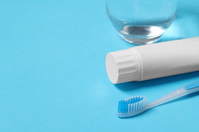 Plastic toothbrush with paste and glass of water on light blue background, closeup. Space for text