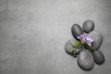Photo of Spa stones and freesia flowers on grey table, flat lay. Space for text