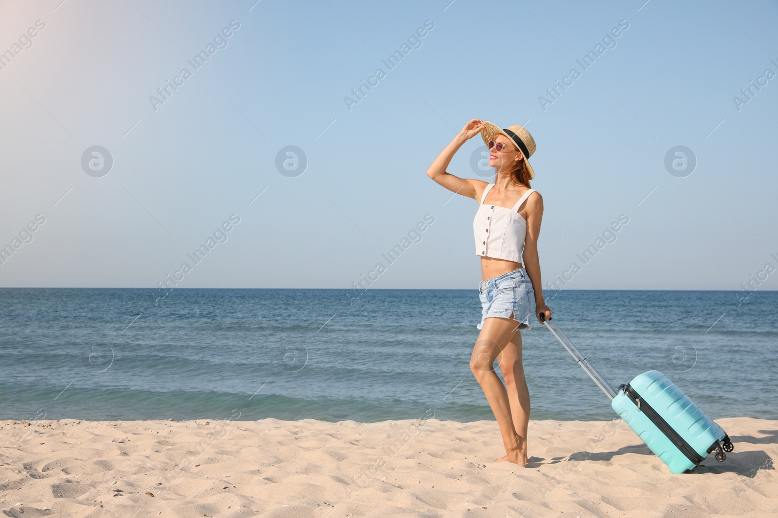 Photo of Beautiful woman with suitcase on sandy beach near sea