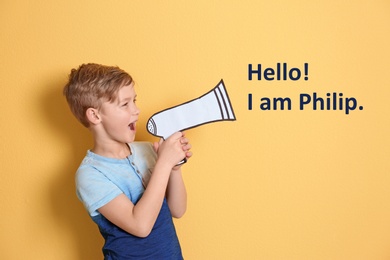 Cute little boy saying Hello! I Am Philip using paper megaphone on yellow background