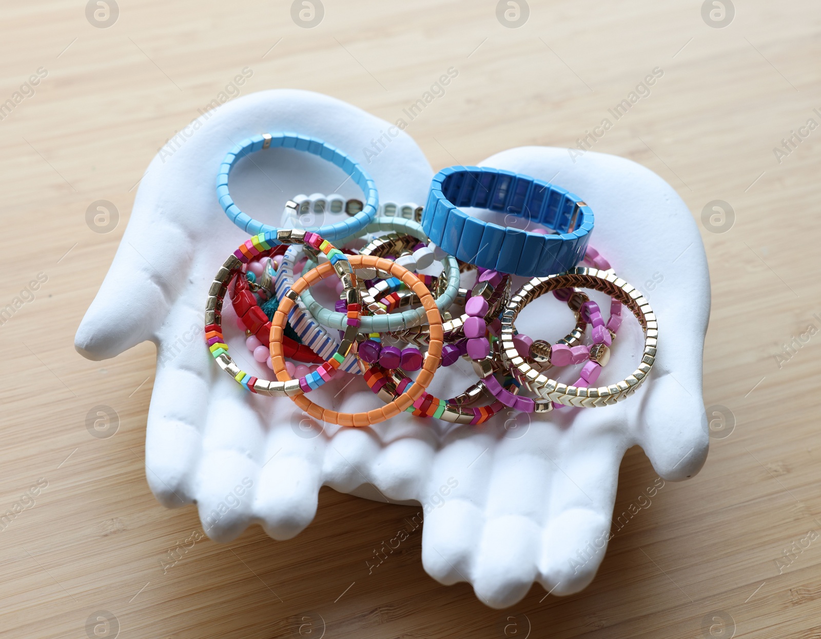 Photo of Ceramic hand stand with many stylish bracelets on wooden table