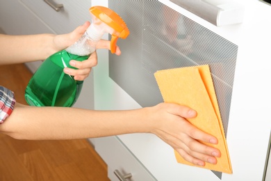 Woman cleaning electric oven with rag and detergent in kitchen, closeup