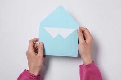 Woman holding letter envelope with card at white table, top view. Space for text