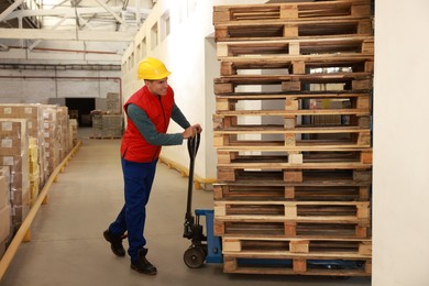 Worker moving wooden pallets with manual forklift in warehouse