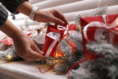 Woman making Christmas advent calendar, focus on paper bag with gift