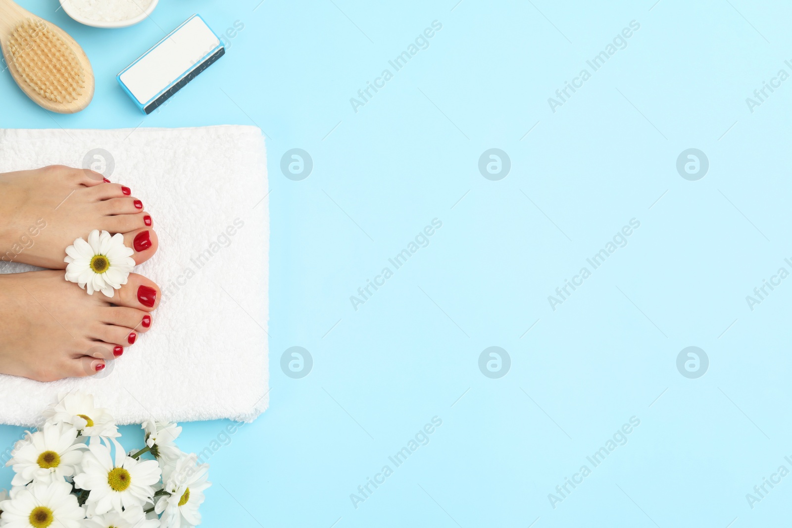 Photo of Woman with stylish red toenails after pedicure procedure and chamomile flowers on light blue background, top view. Space for text