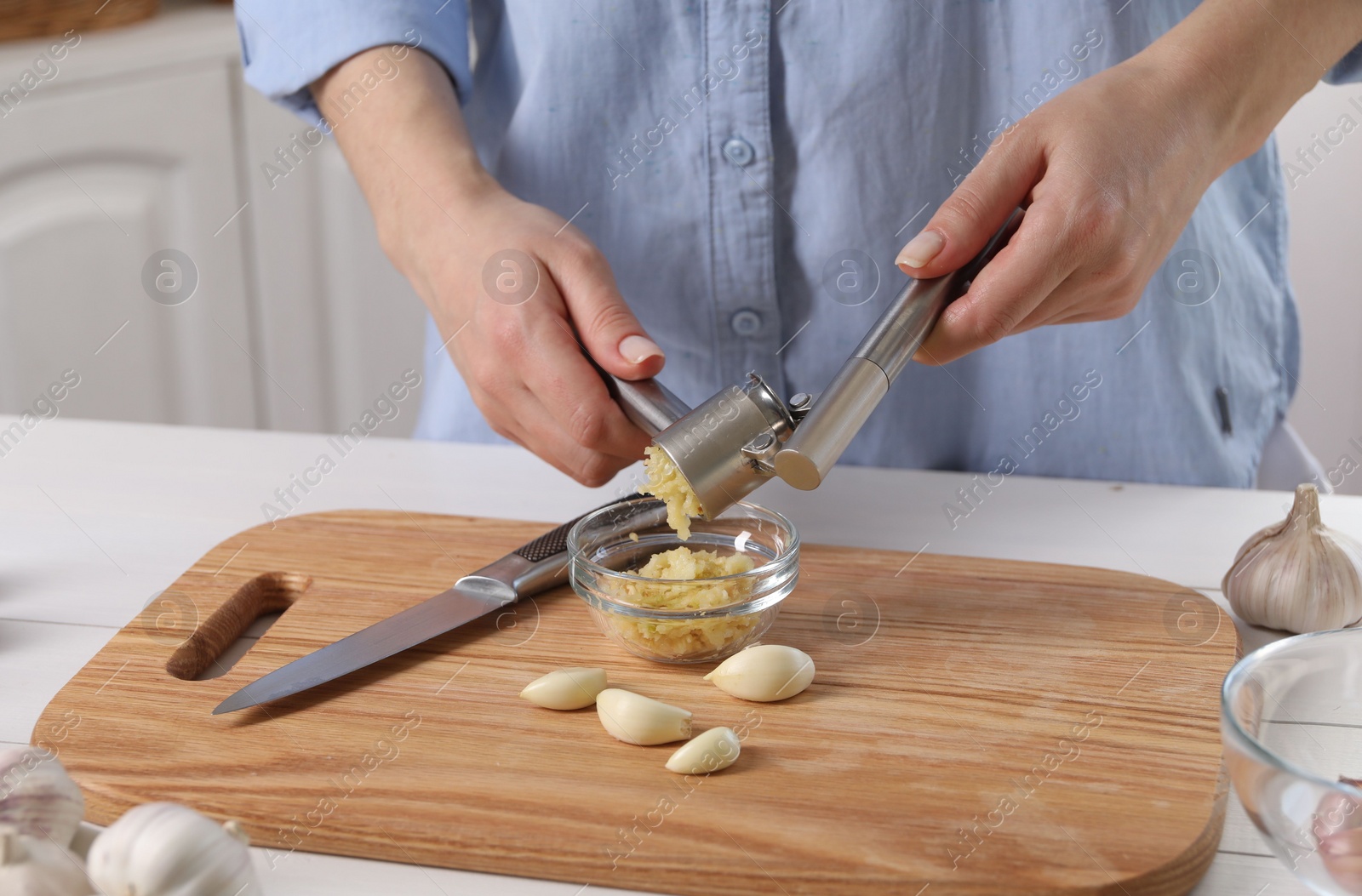 Photo of Woman squeezing garlic with press at white table indoors, closeup