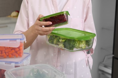 Photo of Woman holding containers with different fresh products in kitchen, closeup. Food storage