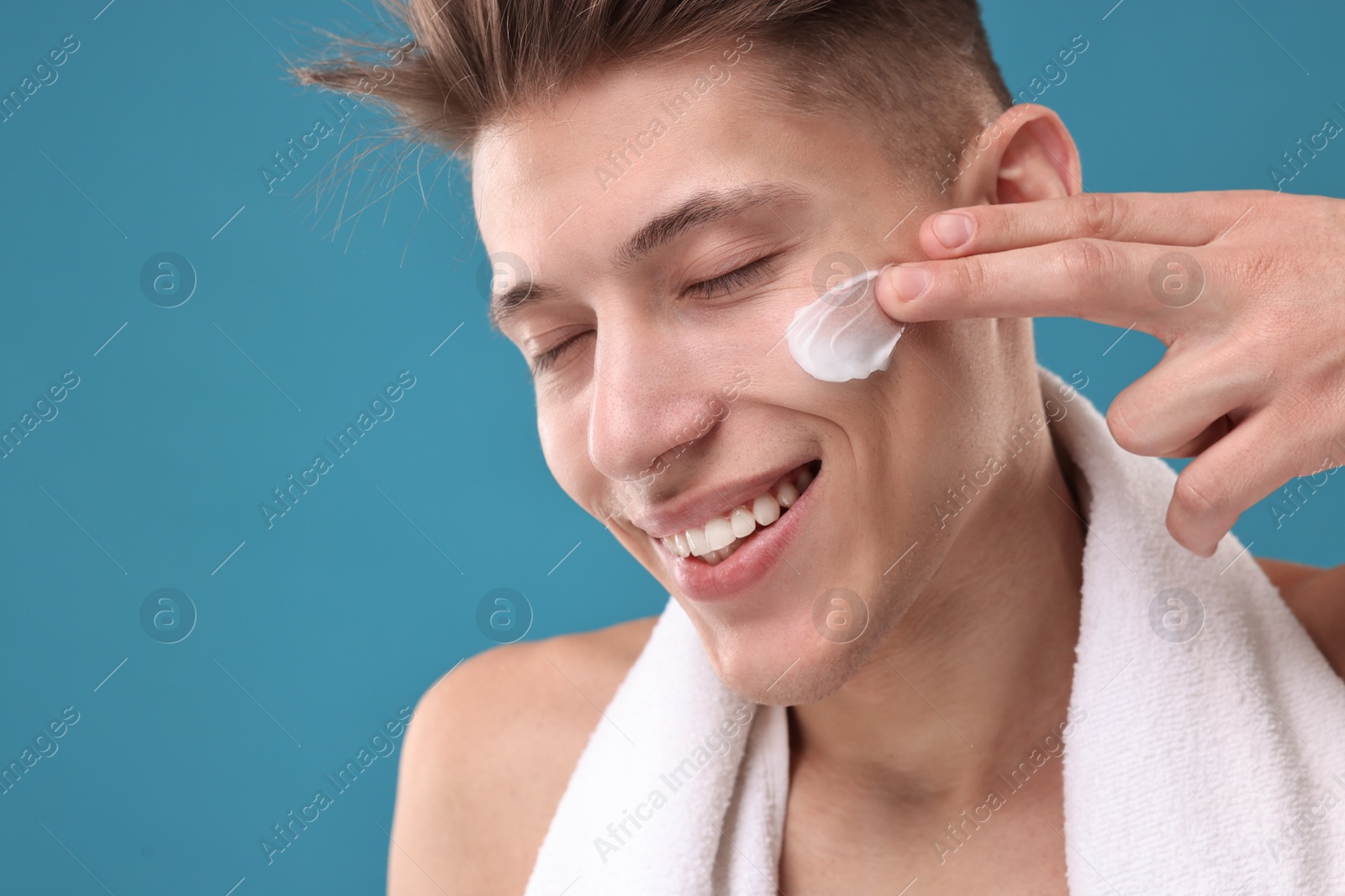 Photo of Handsome man applying moisturizing cream onto his face on blue background, closeup