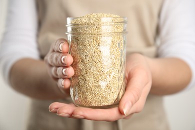 Photo of Woman holding jar with white quinoa on light background, closeup