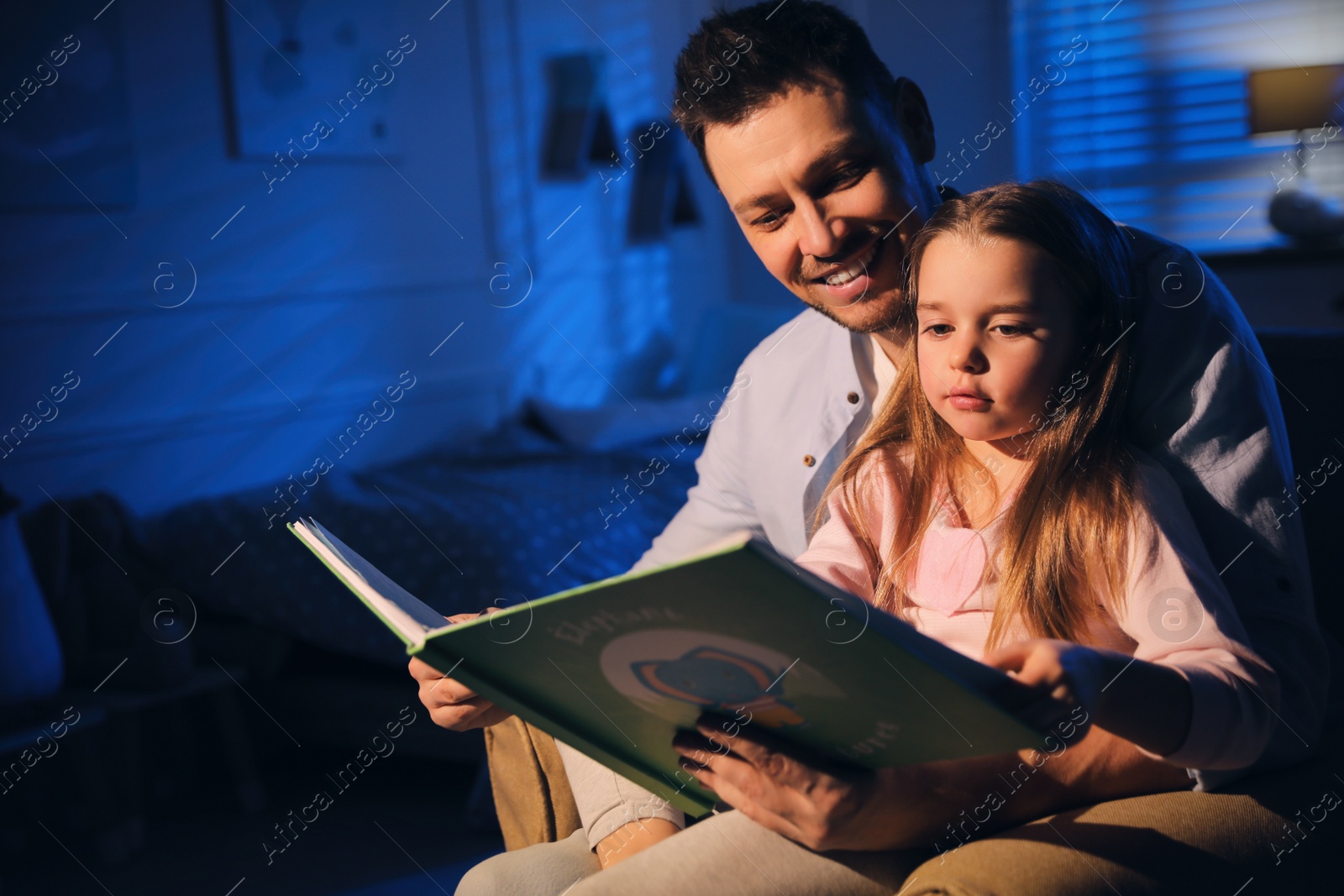 Photo of Father reading bedtime story to his daughter at home