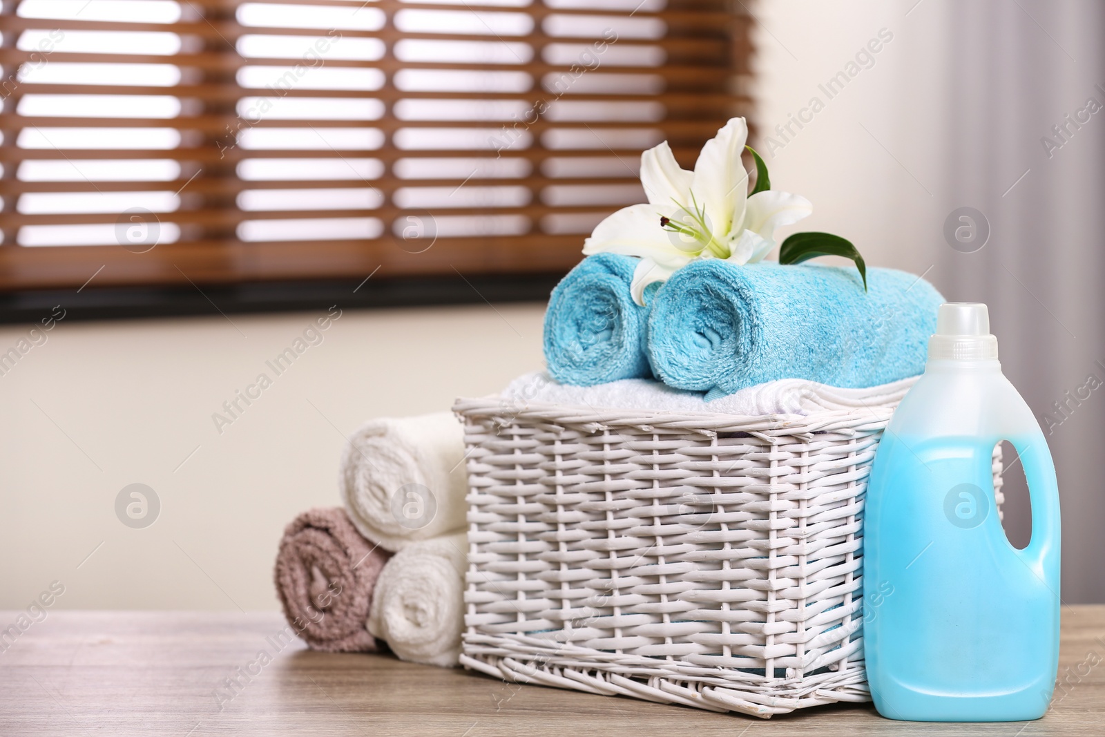 Photo of Basket with towels and detergent on table in room, space for text