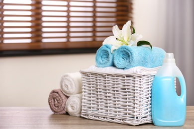 Photo of Basket with towels and detergent on table in room, space for text