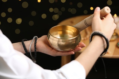 Woman using singing bowl in sound healing therapy on black background, closeup