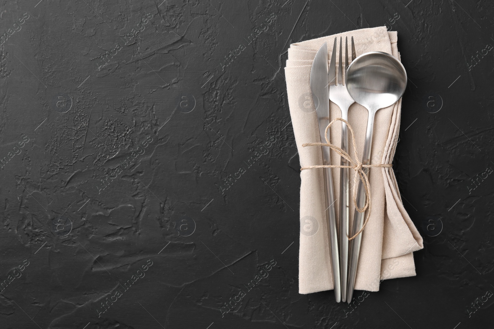 Photo of Set of stylish cutlery and napkin on black table, top view. Space for text