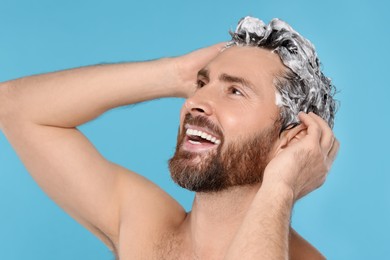 Happy man washing his hair with shampoo on light blue background, closeup