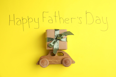Photo of Wooden car, gift box and phrase HAPPY FATHER'S DAY written on yellow background, flat lay