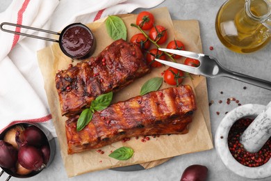 Photo of Tasty roasted pork ribs served with sauce, basil and tomatoes on grey table, flat lay