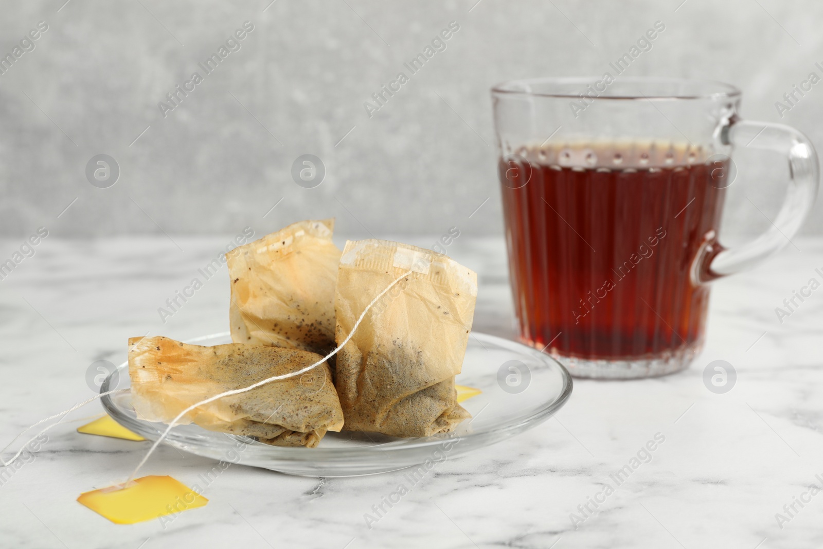 Photo of Saucer with used tea bags and cup of hot drink on white marble table