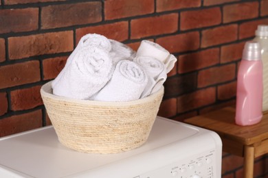 Photo of Terry towels in basket on white washing machine indoors. Laundry room interior design