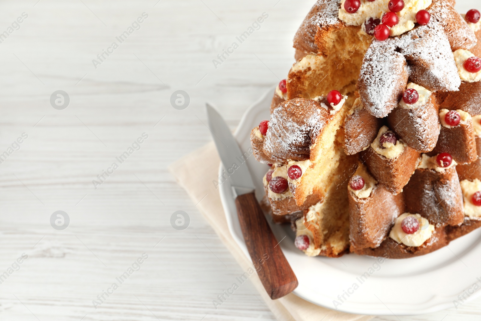 Photo of Delicious Pandoro Christmas tree cake with powdered sugar and berries on white wooden table, closeup. Space for text