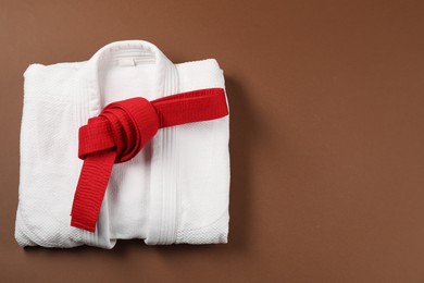 Red karate belt and white kimono on brown background, top view. Space for text