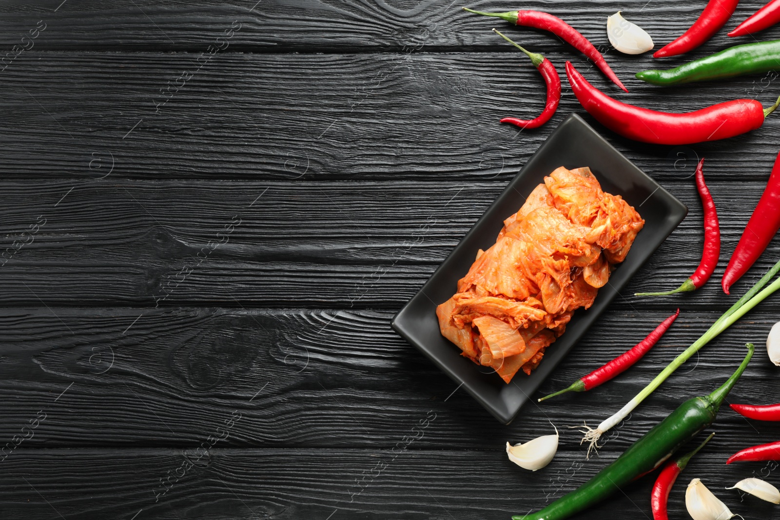 Photo of Delicious kimchi with Chinese cabbage and ingredients on black wooden table, flat lay. Space for text