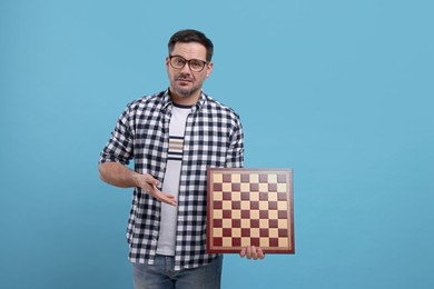 Photo of Adult man showing chessboard on light blue background. Space for text