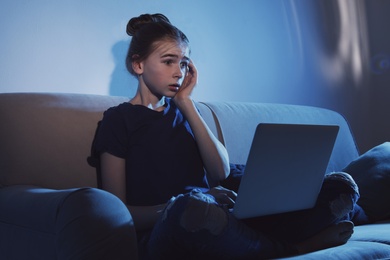 Photo of Shocked teenage girl with laptop on sofa in dark room. Danger of internet