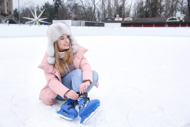 Image of Woman adjusting figure skate while sitting on ice rink. Space for text