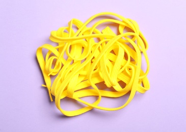 Photo of Yellow shoelaces on lilac background, flat lay