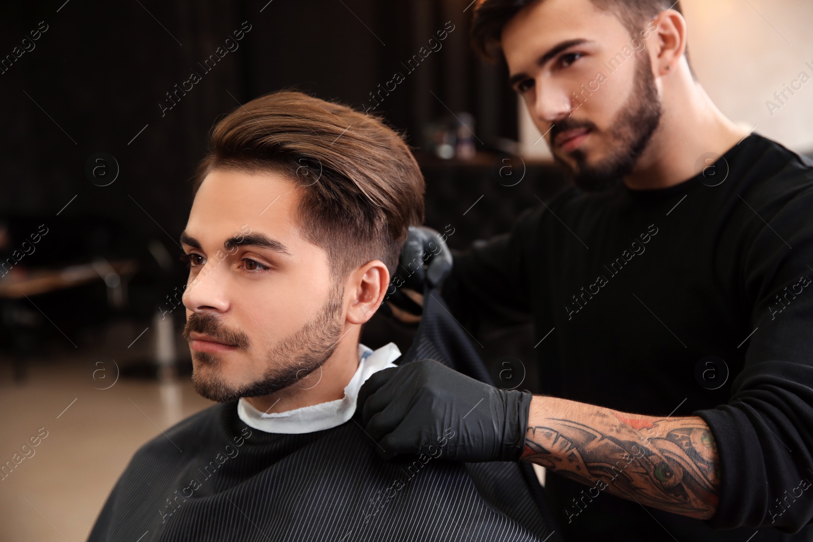 Photo of Professional hairdresser preparing client for shaving at barbershop