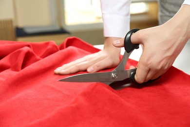 Seamstress cutting red fabric with scissors at workplace, closeup