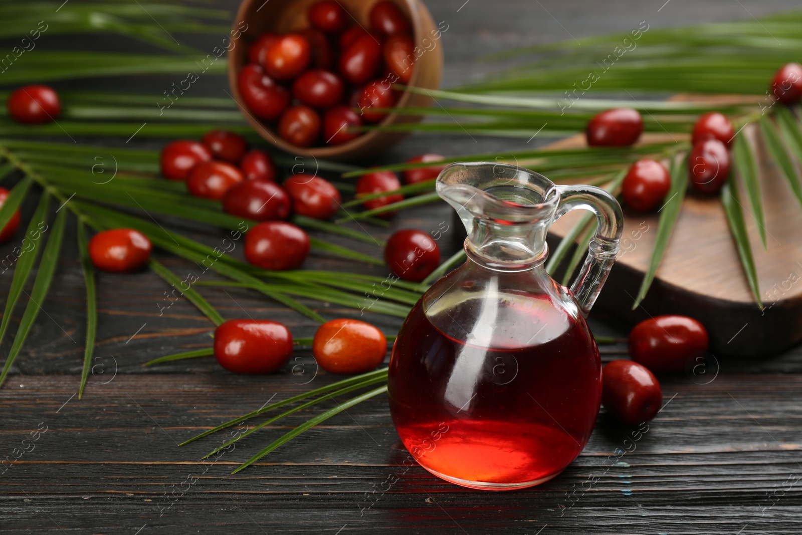 Photo of Palm oil in glass jug, tropical leaves and fruits on wooden table