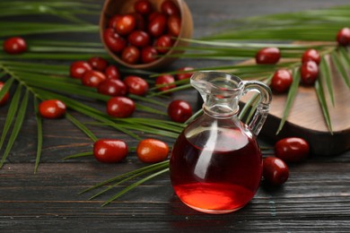 Photo of Palm oil in glass jug, tropical leaves and fruits on wooden table