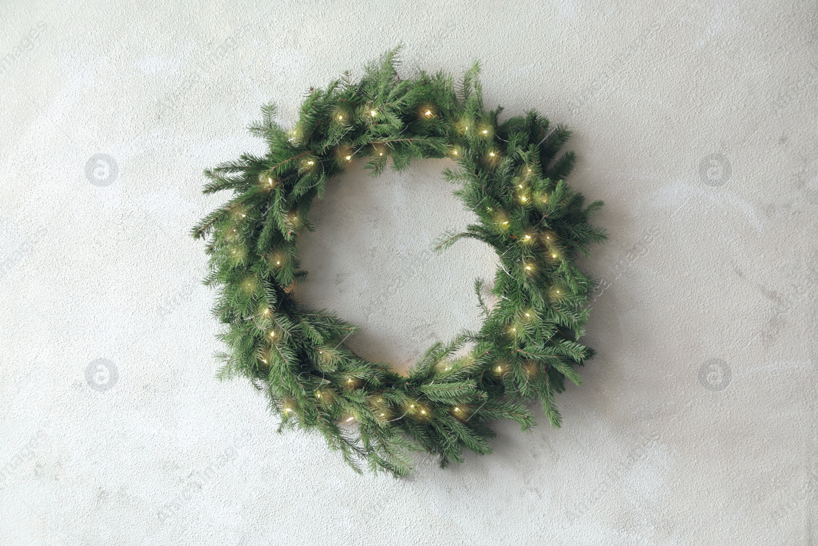 Photo of Beautiful Christmas wreath with festive lights on light wall