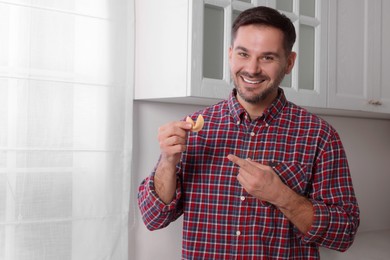 Photo of Happy man holding tasty fortune cookie with prediction indoors. Space for text