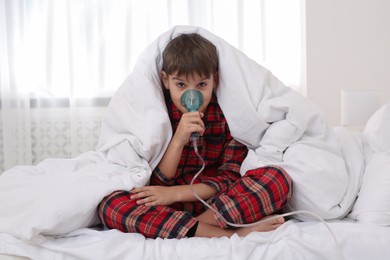 Boy using nebulizer for inhalation on bed at home