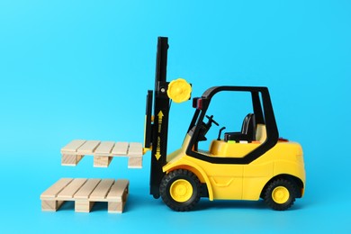 Toy forklift and wooden pallets on light blue background