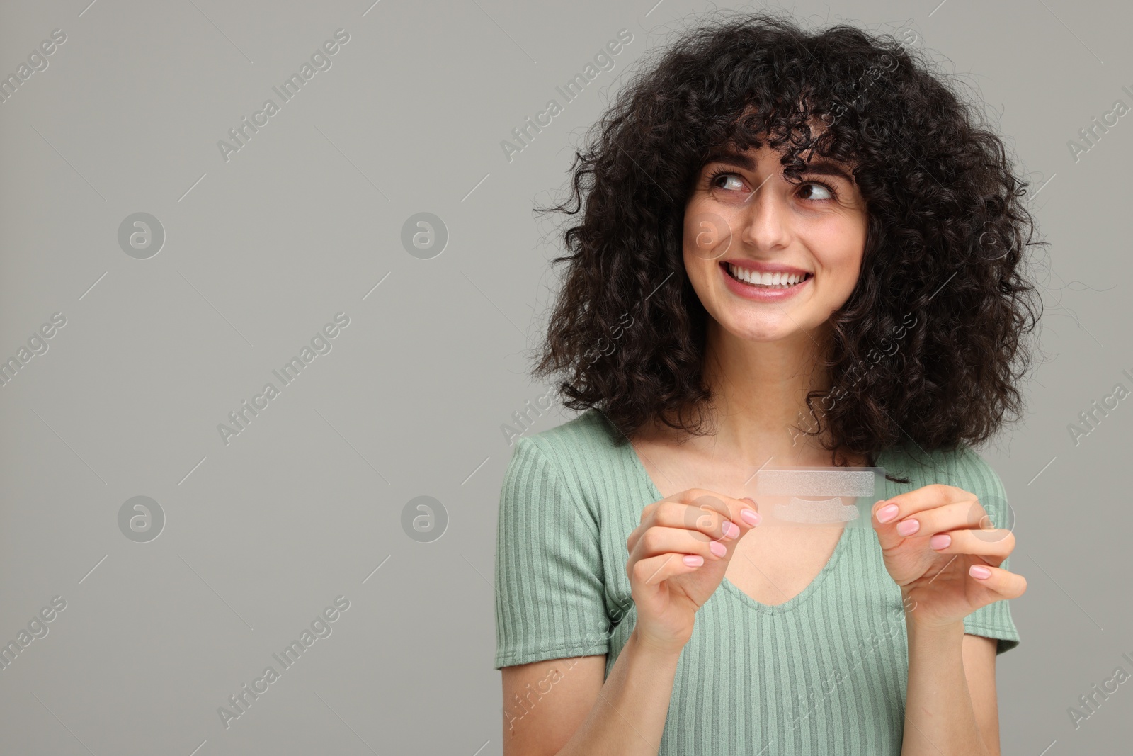 Photo of Young woman holding teeth whitening strips on grey background, space for text