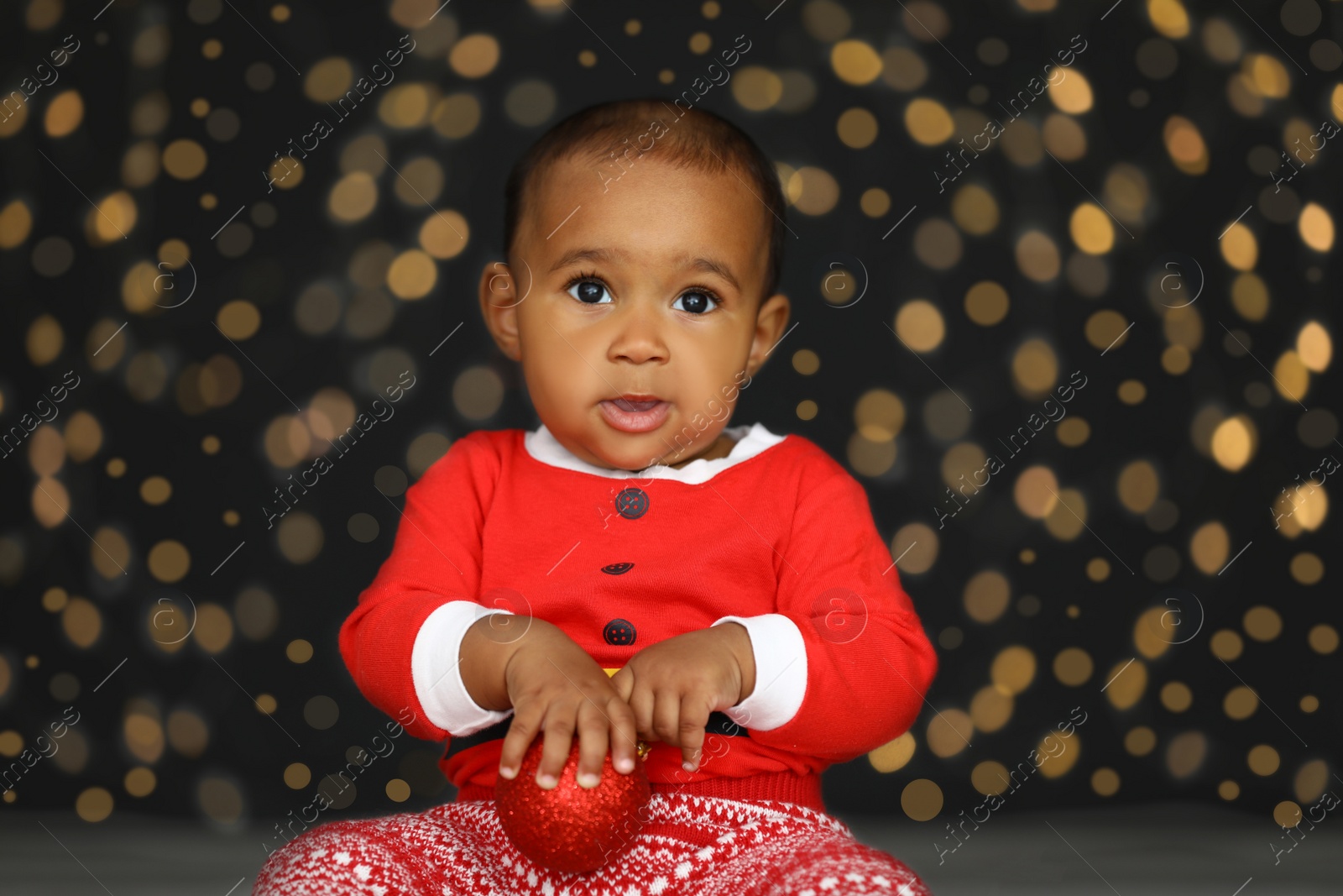 Image of Cute little African American baby with Christmas ball and blurred lights on dark background