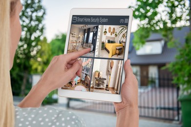 Image of Woman using smart home security system on tablet computer near house outdoors. Device showing different rooms through cameras